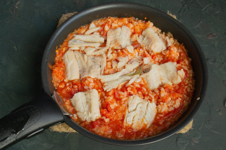 Перемешиваем томатный соус с рисом, солим и выкладываем сверху припущенное филе минтая