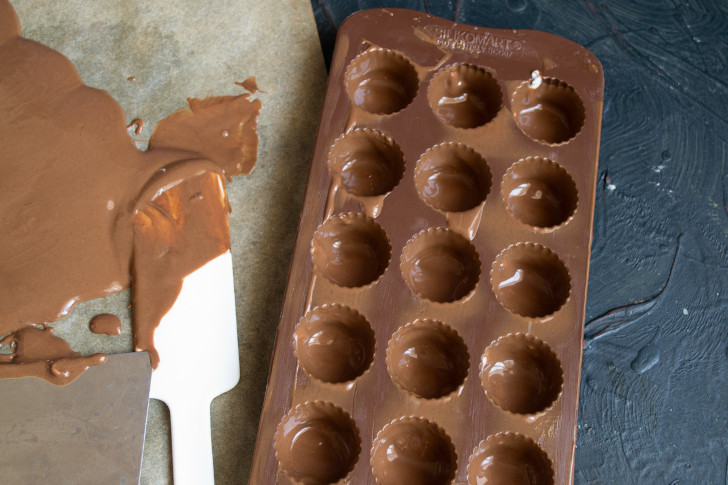 Сливаем шоколад из ячеек, убираем форму в холодильник, шоколад с бумаги соскребаем и снова растапливаем